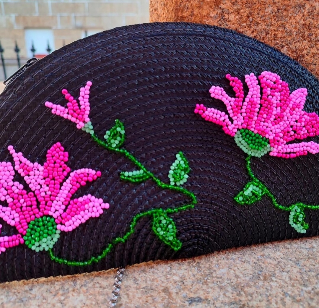 Detalle artesanal de flores bordadas en tonos fucsia sobre un bolso oscuro
